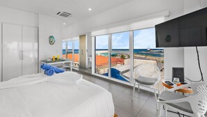 Une chambre d’hôtel avec un grand lit, un bureau avec une chaise, une télévision et un balcon avec vue sur l’océan.