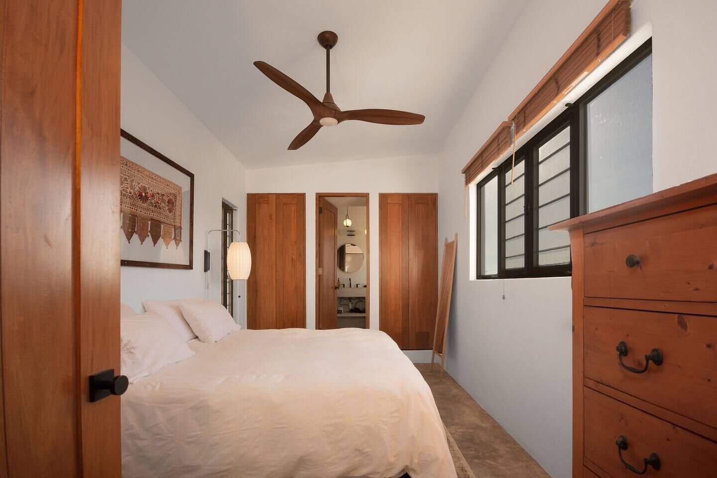 Un dormitorio con cama, armario de madera, ventilador de techo y ventana.