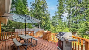 Une terrasse en bois équipée d’un barbecue, d’une table de pique-nique et d’un parasol.
