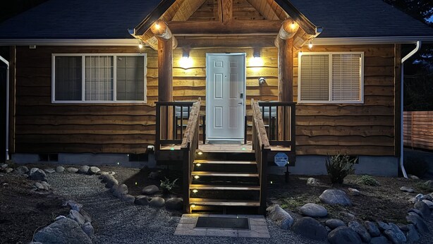 Une cabane en rondins avec un porche à l’avant, une porte et deux fenêtres.