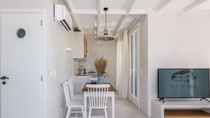 Een moderne keuken met witte kasten, een eethoek met een houten tafel en witte stoelen, en een televisie waarop 'Kuma Bay' te zien is.