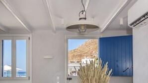 Een knus woongedeelte met een kitchenette, een eethoek met tafel en stoelen, een bank met decoratieve kussens, en uitzicht op de zee door grote ramen.