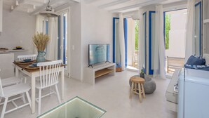 Een moderne keuken met witte kasten, een eettafel met witte stoelen, een televisie en een groot raam met blauwe gordijnen.