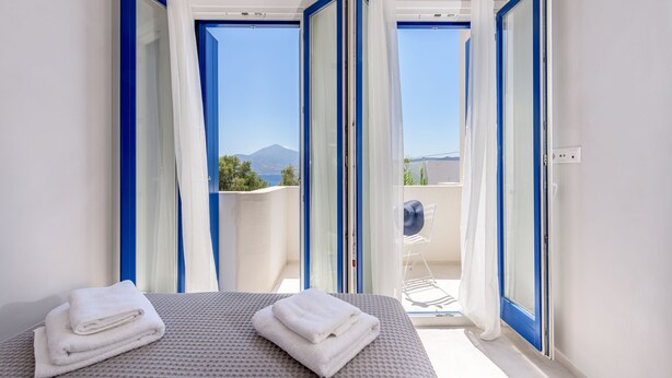 Een hotelkamer met een bed, twee handdoeken en uitzicht op een balkon met een stoel en een tafel.