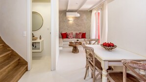 Un intérieur moderne avec un escalier en bois, un coin repas avec une table et des chaises blanches, un canapé avec des coussins rouges et un grand miroir.