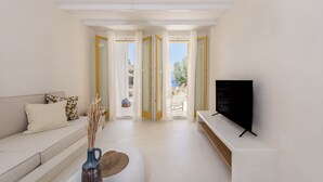 Una sala de estar moderna con un sofá, un televisor de pantalla plana y vistas al exterior a través de puertas abiertas.