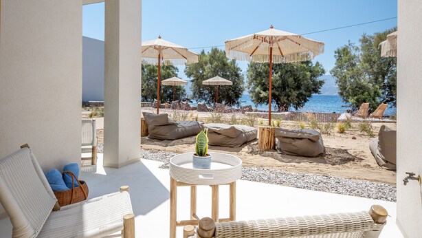 Un patio con mobiliario de mimbre, una mesa pequeña con una planta y sombrillas con vista a la playa.