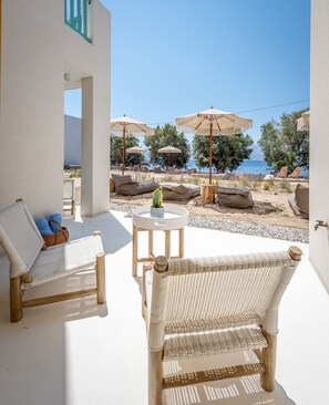 Un patio con mobiliario de mimbre, una mesa pequeña con una planta y sombrillas con vista a la playa.
