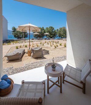 A balcony with wicker furniture, a small table with a potted plant, and a view of the beach and sea. - KLIMA BAY Beachfront Boutique Houses (Orange) (Milos)