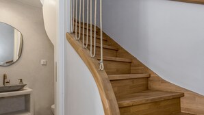 Un escalier moderne avec des marches en bois et une rampe en corde, menant à une salle de bain équipée d’un lavabo et d’un miroir.