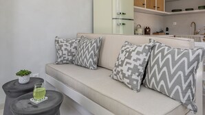Un salon moderne avec un canapé, deux tabourets noirs et une petite table sur laquelle se trouvent une plante et un verre d’eau.