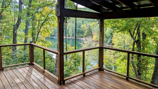 Terraza de madera con barandilla metálica que da a un lago rodeado de árboles.