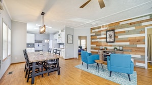 Un amplio salón con una mesa de comedor de madera, sofás azules y una cocina al fondo.