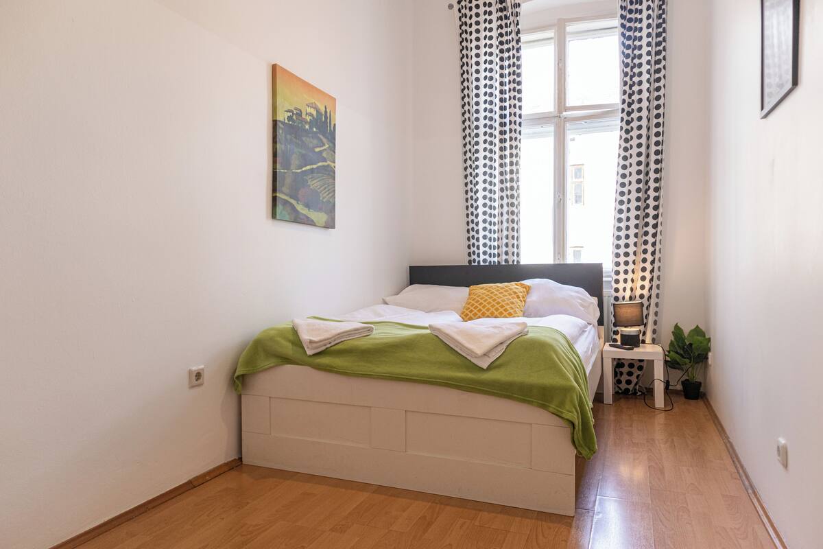 A bedroom with a bed, a nightstand, a lamp, and a window with curtains.