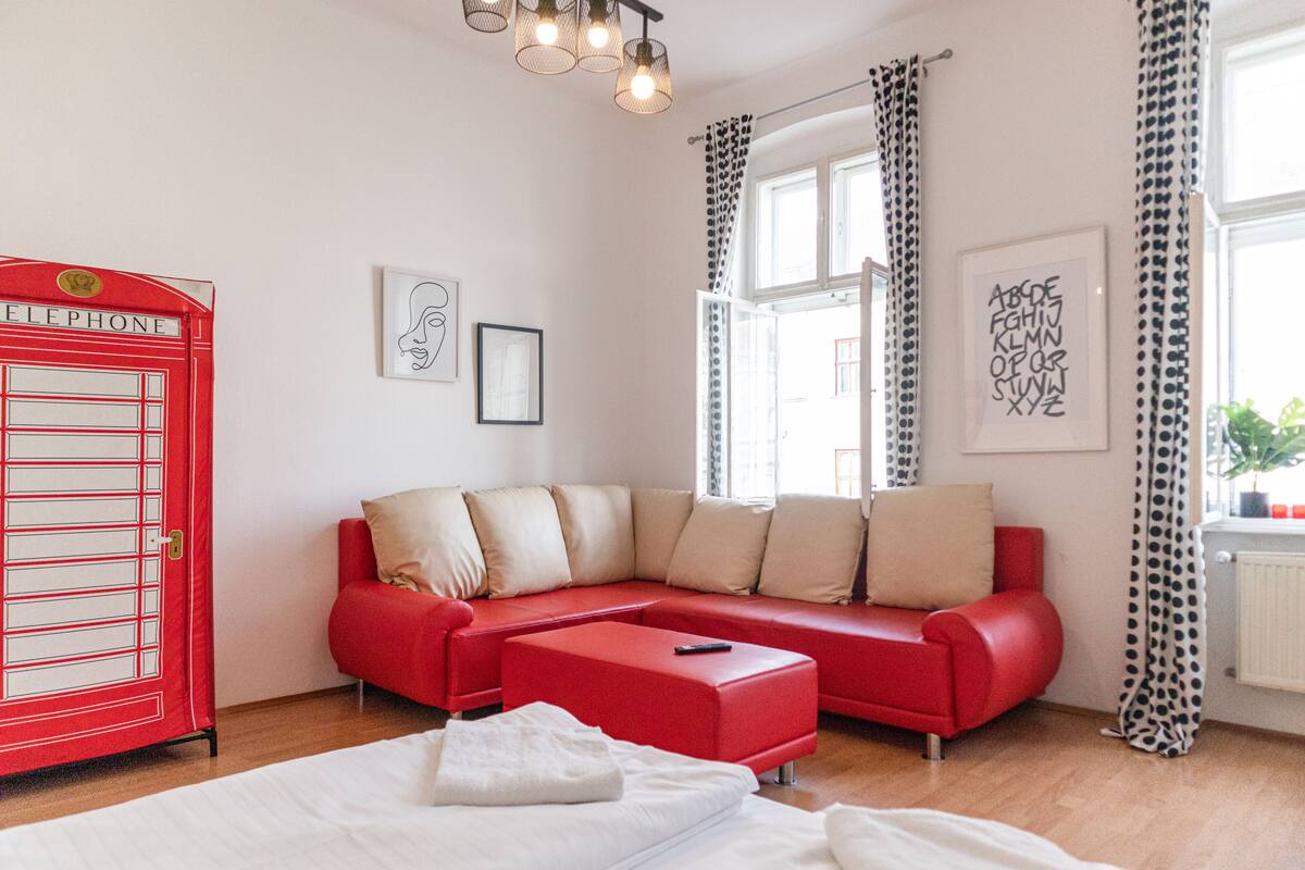A modern living room with a red sofa, a white bed, and a red telephone booth.