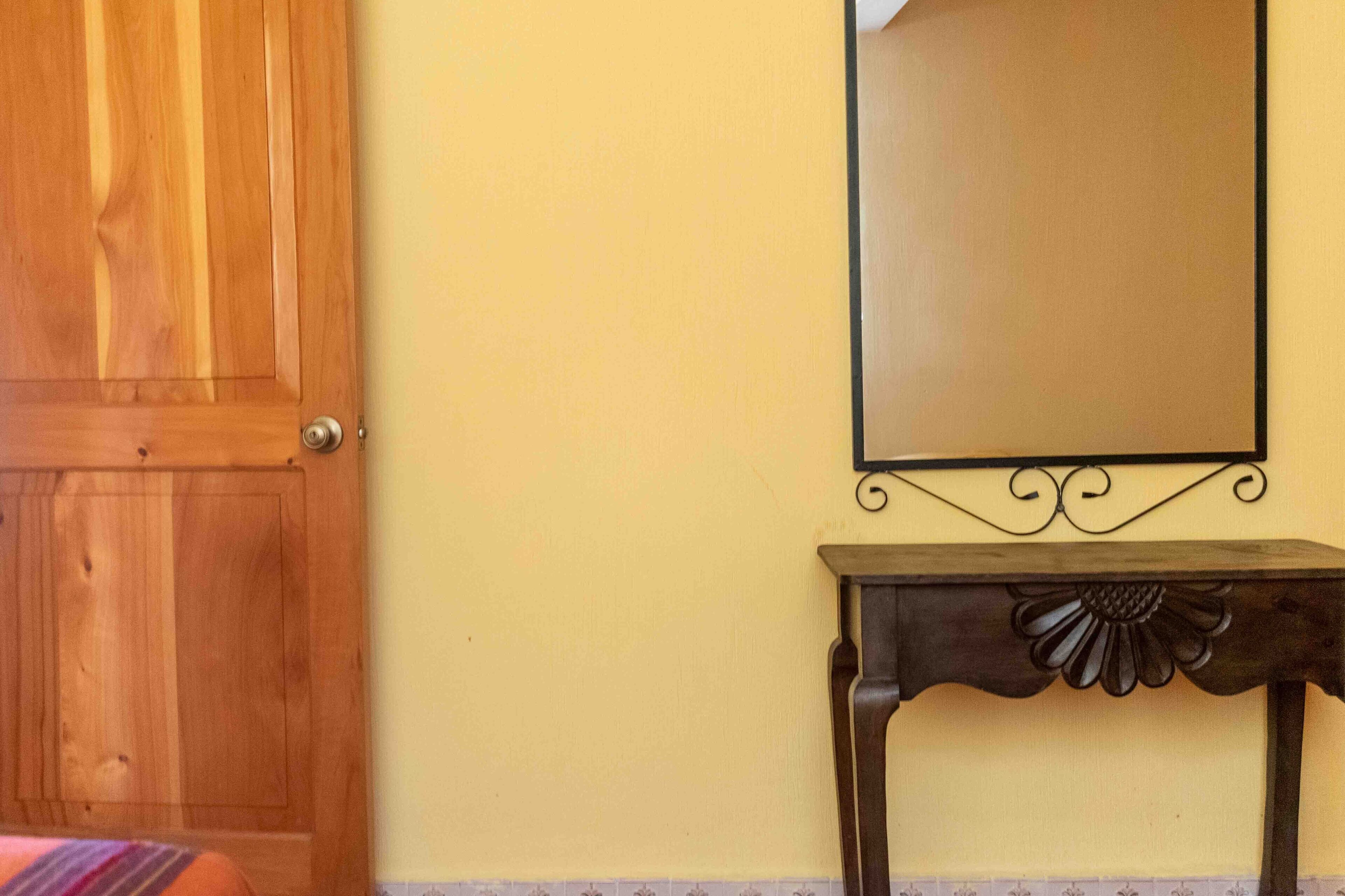Una puerta de madera, un espejo en la pared y una pequeña mesa con un detalle decorativo.