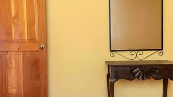 Una puerta de madera, un espejo en la pared y una pequeña mesa con un detalle decorativo.