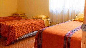Habitación de hotel con dos camas, cada una con una colcha naranja a rayas, una cama con una almohada amarilla y una ventana con cortinas de encaje.
