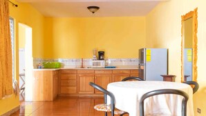 Una cocina con armarios de madera, una mesa con sillas, un refrigerador y un microondas.