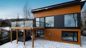 Une maison moderne à deux étages, dotée de grandes fenêtres et d’une façade en bois.