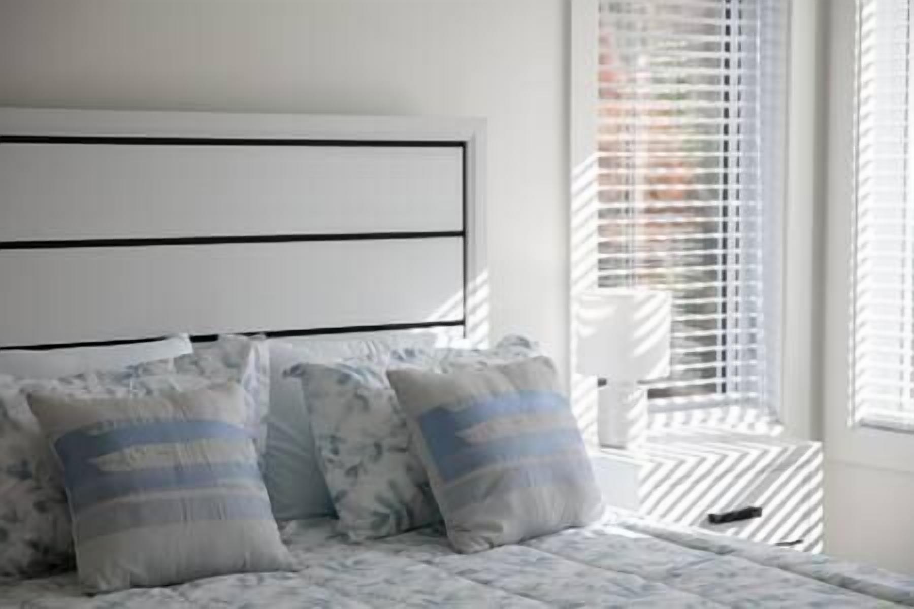 A bedroom with a bed, pillows, and a window with blinds.