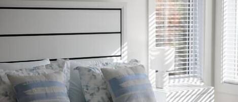 A bedroom with a bed, pillows, and a window with blinds.