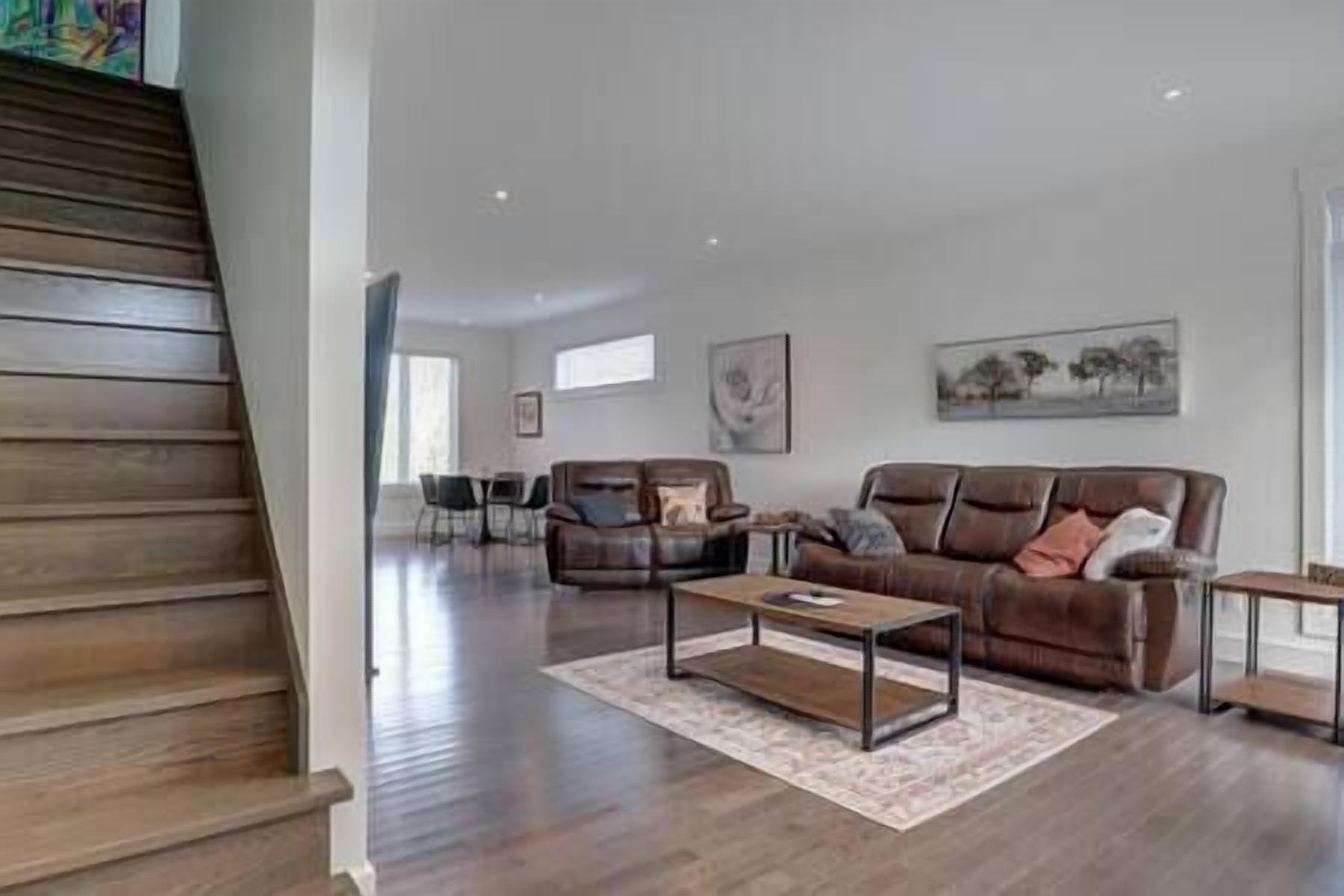 Un vaste espace de vie comprenant un canapé en cuir marron, une table basse et une table à manger avec des chaises.