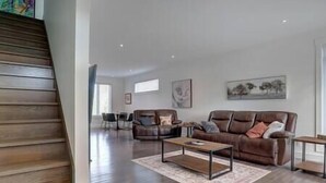 A spacious living area with a brown leather sofa, a coffee table, and a dining table with chairs. - Hôtel à la maison - Le Faucon Azuré, golf et ski (Potton)