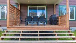 A covered outdoor area with a table and chairs, a barbecue grill, and a wooden staircase leading up to the entrance. - Hôtel à la maison - Le Faucon Azuré, golf et ski (Potton)