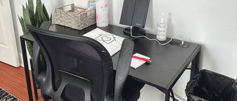 Un pequeño espacio de oficina con escritorio, silla, computadora, calendario y un cubo de basura.