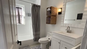 A bathroom with a toilet, sink, and bathtub. There is a window with curtains, a towel rack, and a mirror. - 💎 Chic Private Room 🛜 Fast Wi-Fi 👣Near LIRR & Shops (Hicksville)