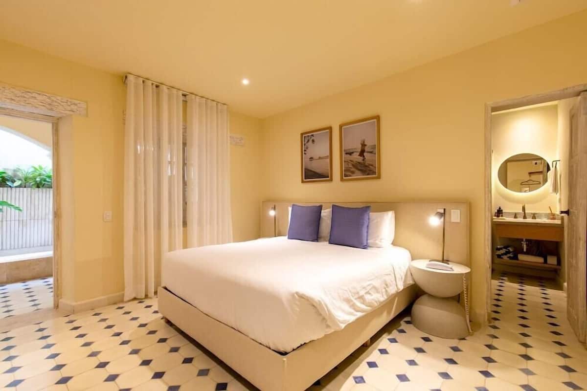 Un dormitorio con cama, mesitas de noche, un espejo y vistas al exterior.