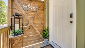 Une clôture en bois avec une pancarte « Bienvenue », une lanterne et une plante en pot près d’une porte blanche.