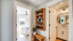 Un couloir avec un banc en bois, une étagère ornée d’objets décoratifs et une vue sur une chambre à coucher.