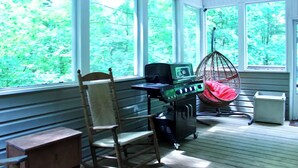 Une pièce dotée de grandes fenêtres, d’une chaise en bois, d’une chaise suspendue et d’un barbecue.