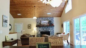 Un salon spacieux avec une cheminée, des meubles en osier et une pancarte « Bienvenue » posée sur une table.