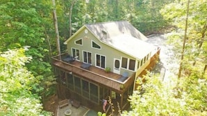 Une cabane à deux étages dotée d’une terrasse, entourée d’une forêt dense.