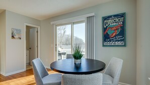 A dining area with a round table, two grey chairs, a potted plant, and a wall poster advertising Connecticut lobster. - Niantic Duplex w/ Deck < 1 Mi to Beach + Boardwalk (Niantic)
