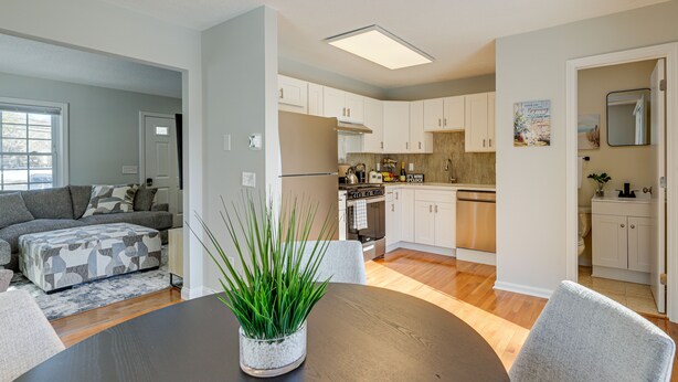 A modern kitchen with white cabinets, a central island, and a dining area with a round table and chairs. - Niantic Duplex w/ Deck < 1 Mi to Beach + Boardwalk (Niantic)