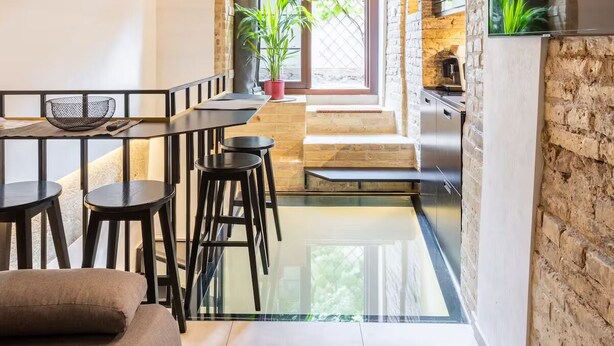 A modern kitchen with a stone wall, a dining area with a glass table, and a large window. - Cuddle Puddle  (Vilnius)