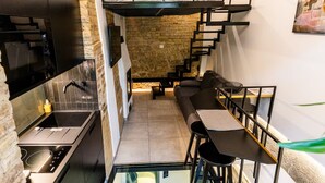 A modern kitchen with a stone wall, a glass dining table, and a staircase leading to a loft area. - Cuddle Puddle  (Vilnius)