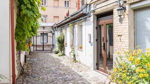 A narrow cobblestone street flanked by buildings with white facades and a metal gate. - Cuddle Puddle  (Vilnius)