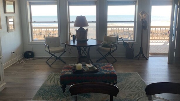 Une pièce avec vue sur la plage, une table avec des chaises, une lampe et un banc.