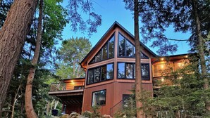 A modern cabin with a large deck, surrounded by trees and rocks. - New 5 bed 4 bath cottage on Turtle Lake, Privacy! (Seguin)