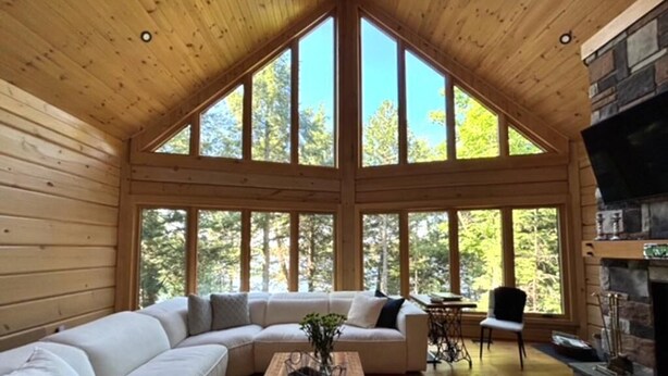 A log cabin interior with a large wooden ceiling, a stone fireplace, and a large windowed wall. - New 5 bed 4 bath cottage on Turtle Lake, Privacy! (Seguin)