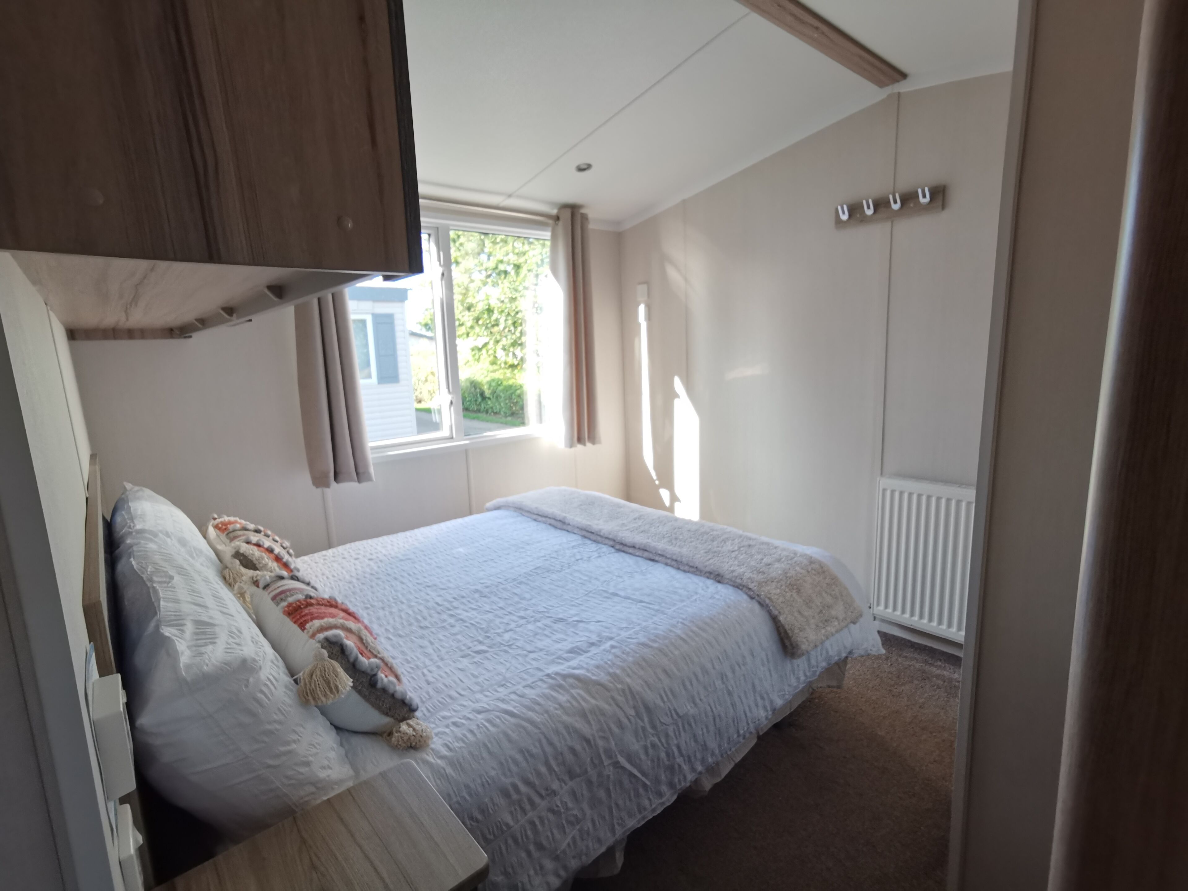 A bedroom with a bed, a wooden wardrobe, a window with curtains, and a radiator.