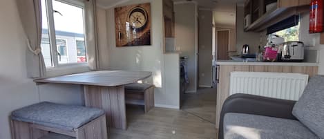 A modern kitchen with wooden cabinets, a dining area with a bench, and a grey sofa.