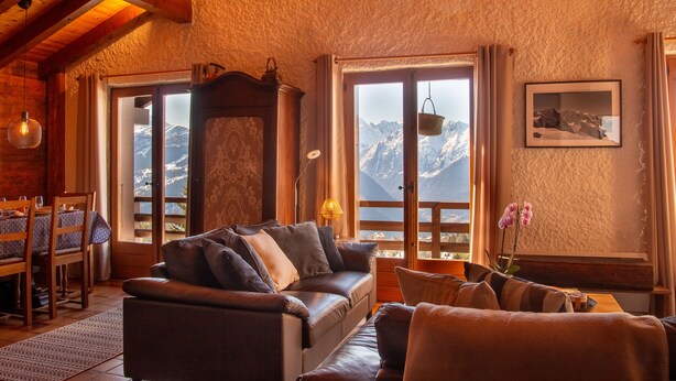 Un accogliente soggiorno con una poltrona in pelle, un tavolo da pranzo con sedie e vista sulle montagne attraverso ampie finestre.