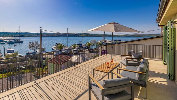 Eine Terrasse mit Sitzgelegenheit, Blick auf Boote auf dem Wasser und einen klaren Himmel.
