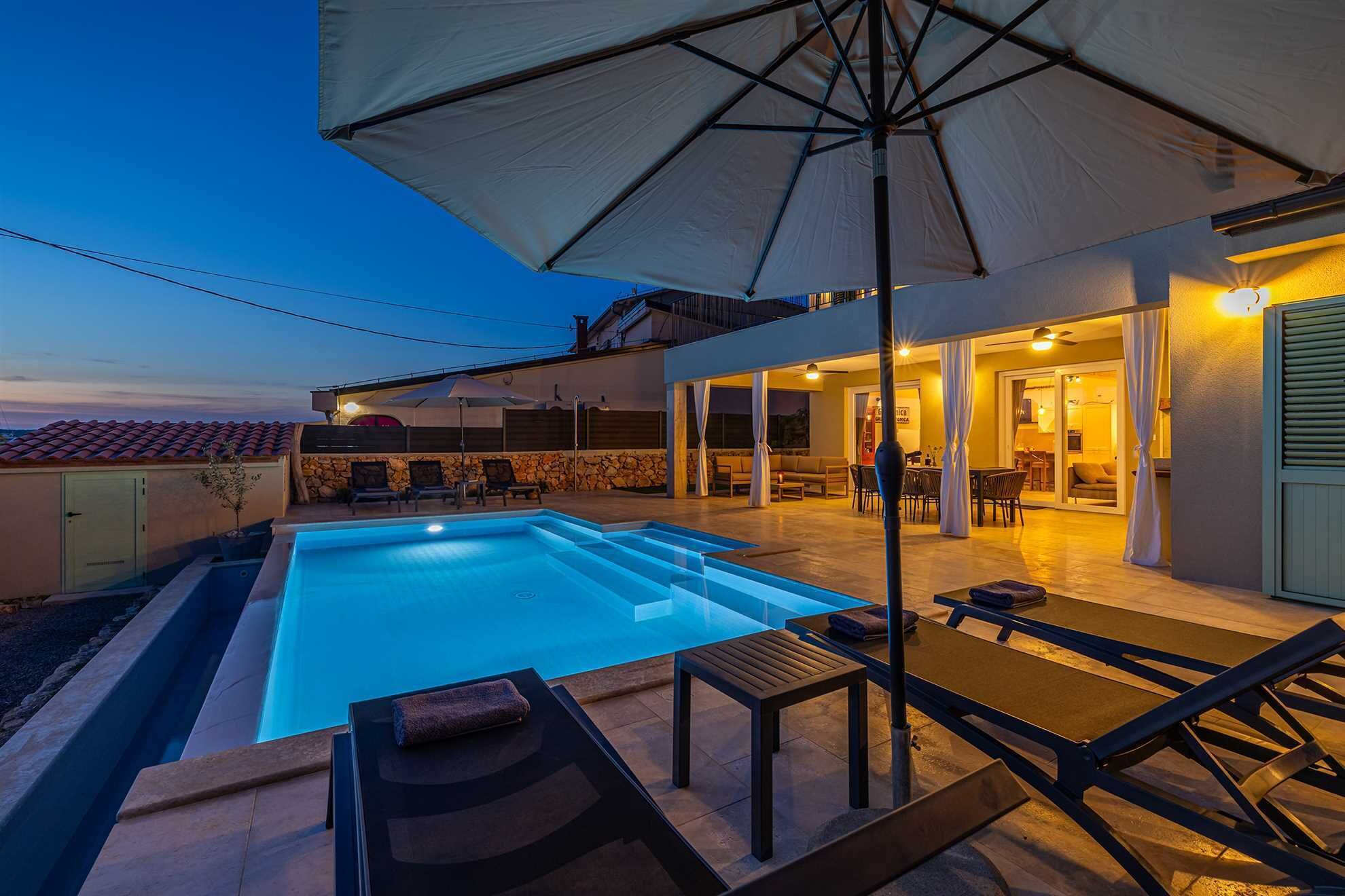 Piscina com espreguiçadeiras e guarda-sóis, parede de pedra e área de varanda coberta com assentos.
